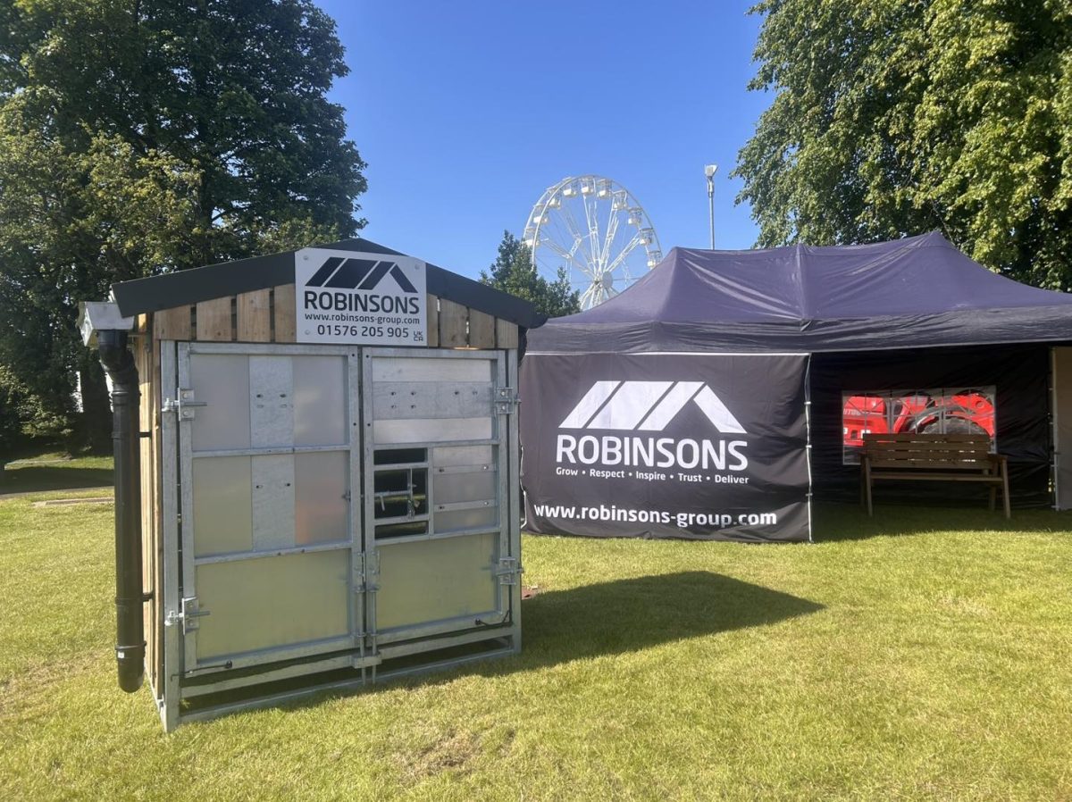 An image of a section of the Robinsons stand at the Highland Show. Picture features a ferris wheel in the background, and a black gazebo, alongside a small shed, in the foreground. Both feature the Robinsons logo.